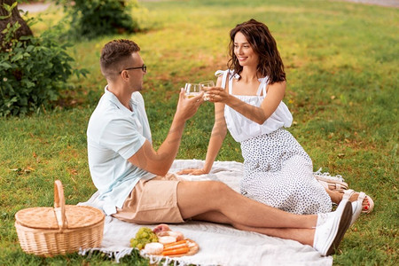 休闲和人的概念快乐的夫妇与饮料和食物在夏季公园野餐。一对幸福的情侣在夏季公园野餐