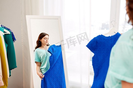 服装时尚和人概念-沉思的加上有蓝色衣服的妇女在镜子的尺寸在家。沉思加上大小妇女与蓝色连衣裙在镜子