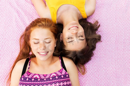 夏季时尚，休闲和人的概念—微笑的少女或朋友躺在野餐毯。微笑的少女躺在野餐毯子