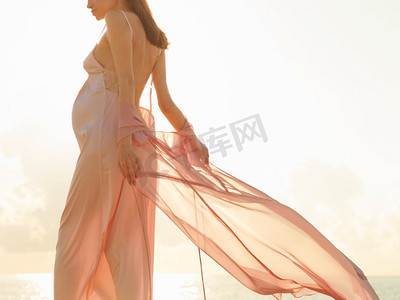 户外大气生活方式肖像美丽的孕妇粉红色连衣裙。美好的早晨。海滩上的日出。美容和时尚