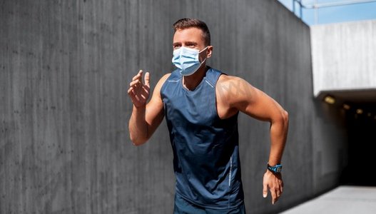 新冠肺炎培训摄影照片_健身、运动和健康理念--戴着医用口罩的年轻人在户外跑步。一名戴着医用口罩的年轻人在户外跑步