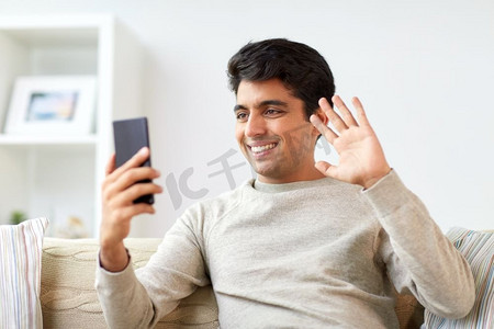 技术、人与沟通理念--智能手机在家视频通话的快乐男士。开心的男人在家里用智能手机进行视频通话