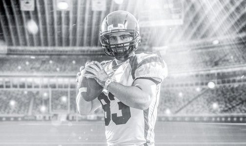 一名四分卫美式橄榄球运动员在灯光和照明弹的大型现代体育场上抛出孤立的球