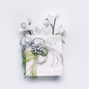 白色桌面背景上有绿丝带和兰花的纸质礼品袋，俯视