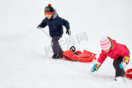 爬雪山摄影照片_童年，雪橇和季节概念—快乐的小孩子与雪橇爬雪山在冬天。孩子们带着雪橇爬雪山在冬天