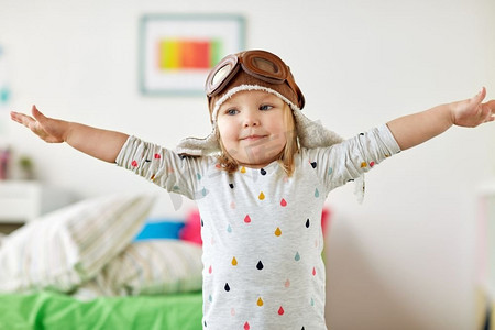 童年，想象和梦想的概念--快乐的小女孩戴着飞行员帽在家里玩游戏。戴着飞行员帽的快乐小女孩在家里玩耍