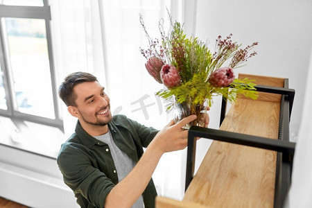 家居装修，装饰和人们的概念—快乐的微笑的人把鲜花放在花瓶架子上。男人用花瓶装饰家