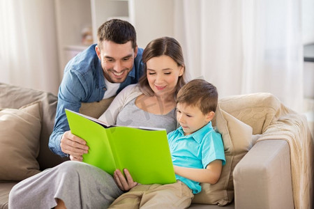 人与家庭观念-快乐的父母和小儿子在家里的沙发上看书。快乐的家庭在家读书