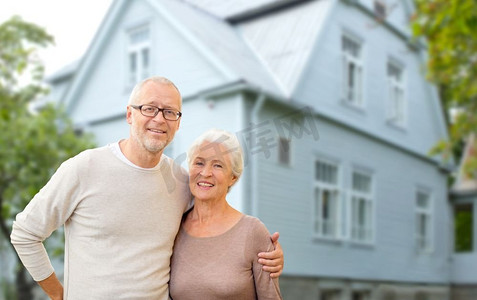 老年，住宿和房地产概念—愉快的高级夫妇拥抱超过房子背景。愉快的高级夫妇拥抱在房子背景