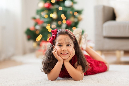 圣诞节、节日和童年的概念--快乐的小女孩躺在家里的地板上。圣诞节快乐的女孩躺在家里的地板上