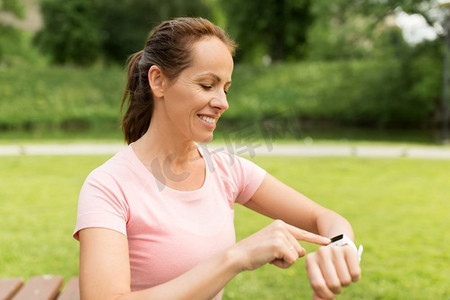 运动和科技概念-公园里戴着智能手表或健身追踪器的微笑女性。公园里戴着智能手表或健身追踪器的女子
