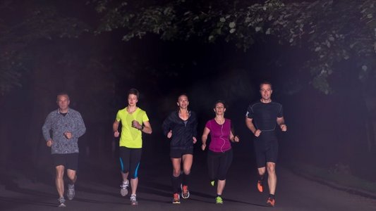 跑步运动的人摄影照片_跑步队在夜间训练。一群健康的人在城市公园慢跑，跑步者团队在夜间训练