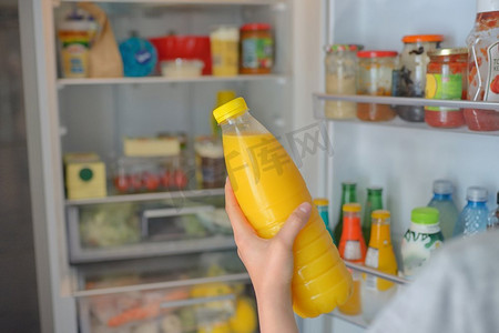 十几岁的女孩从开着的冰箱里拿出橙汁。十几岁的女孩喝橙汁