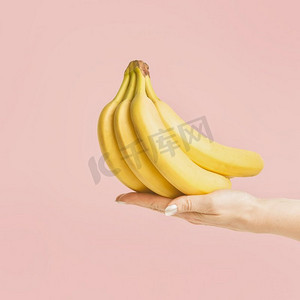 女性手持一串香蕉，以淡粉色为背景，正视