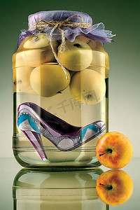 一只保存在装有苹果的玻璃瓶里的时尚高跟鞋的特写。