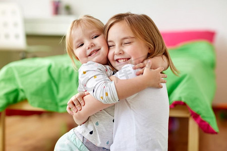 小表情摄影照片_童年，家庭，表情和人的概念-快乐的小女孩或姐妹在家里拥抱。快乐的小女孩或姐妹们在家中拥抱