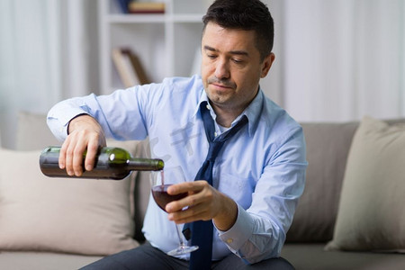 酗酒、酗酒和人的观念——男性酗酒者在家里向玻璃杯倒红酒。在家里把红酒倒在玻璃杯上