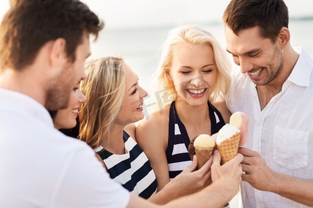吃冰淇淋的女人摄影照片_友谊、休闲和人的概念-一群穿着条纹衣服在海滩上吃冰淇淋的快乐朋友。快乐的朋友在海滩上吃冰淇淋