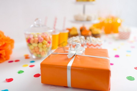 拴五彩丝摄影照片_派对和节日概念-餐桌上橙色包装的生日礼物的特写。派对桌上放着橙色包装的生日礼物