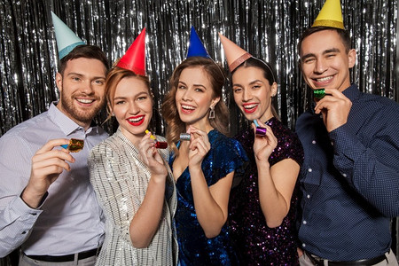 庆祝、娱乐和假期的概念-带着派对吹风机和生日帽的快乐情侣。快乐的情侣和派对吹风机一起玩得很开心