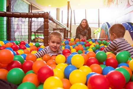 愉快的家庭享受空闲时间年轻的母亲玩与孩子在有五颜六色的球的游泳池在儿童游戏室