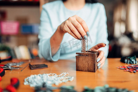 女人手从木箱里掏出一条金属链子，师傅在干活。手工制作的珠宝。针线活、首饰制作