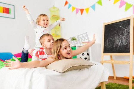 童年、休闲和家庭概念-快乐的小孩子在家里的床上玩得开心。快乐的小孩子们在家里的床上玩得开心