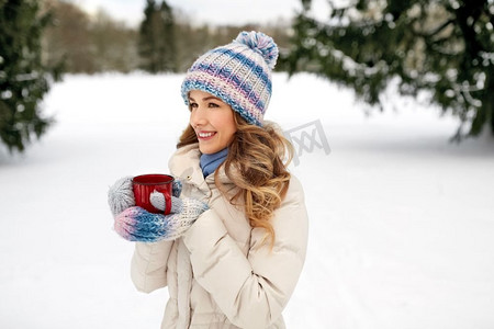 冬季季节摄影照片_人，季节，饮料和休闲概念—快乐的年轻妇女与茶杯户外在冬天。愉快的年轻妇女与茶杯户外在冬天