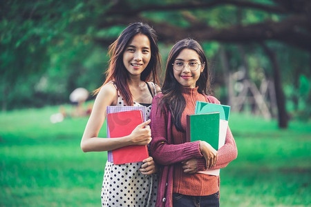 年轻的女学生朋友手里拿着书站在大学公园里。教育理念。