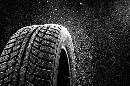 雪扫了一个冬季轮胎罩在黑色背景。雪中的橡胶