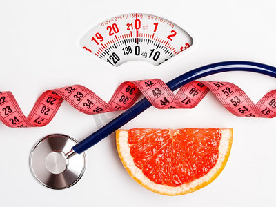 健康饮食的摄影照片_饮食健康饮食体重控制理念。葡萄柚，白鳞片上有卷尺和听诊器