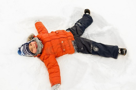 冬季衣服摄影照片_童年，休闲和季节概念—快乐的小男孩冬季衣服做雪天使户外。快乐的小男孩做雪天使在冬天