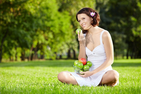 美女坐在草坪上吃苹果，横