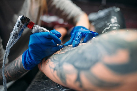 女纹身师用机器在男性肩膀上纹身。专业纹身在沙龙。纹身师通过机器在男性肩膀上纹身