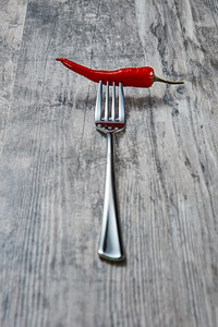 辣椒被刺穿在钢叉上，背景是旧的木制，留有复印空间。老木头背景上的叉子上放着辣红辣椒
