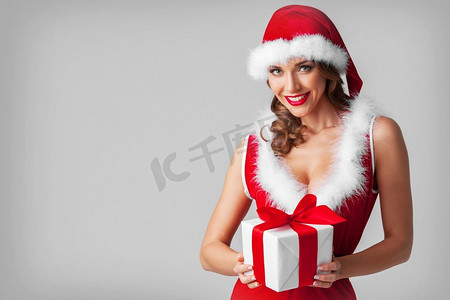 在圣诞老人帽子庆祝圣诞节举行礼物盒的美丽的年轻妇女。妇女在圣诞老人帽与礼物
