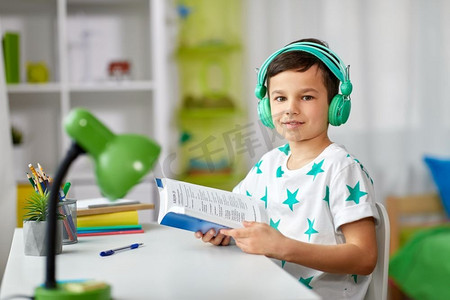 教育，童年和技术概念—快乐的学生在耳机读书在家。男孩在耳机与教科书学习在家里