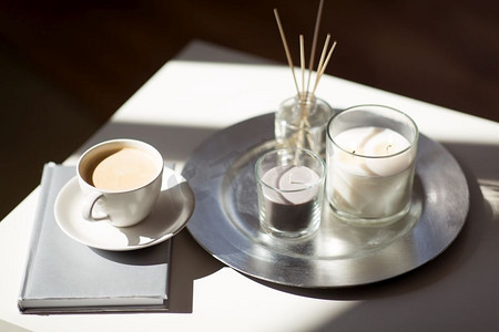香味摄影照片_Hygge和芳香疗法概念—咖啡，蜡烛，书和香气芦苇扩散在桌子上。咖啡，蜡烛和香味芦苇扩散在桌子上