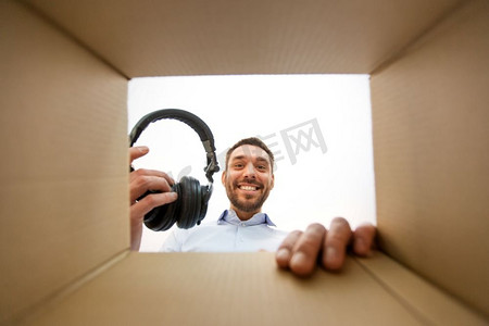 邮件递送和惊喜的概念—微笑的男人从包裹箱里拿出新耳机，从下面。微笑的男人拿着耳机从包裹箱
