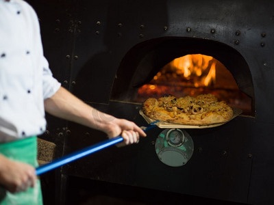 两会特别词摄影照片_厨师用特殊的铲子把热比萨饼从炉子里拿出来。厨师从炉子中取出热披萨