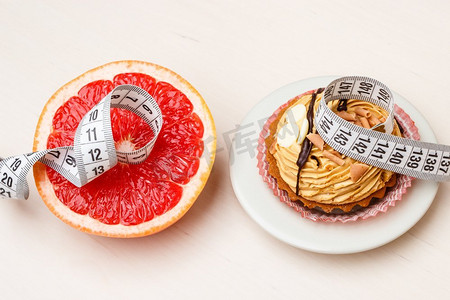 高卡路里摄影照片_选择理念：健康的低卡路里或不健康的高卡路里食物，减肥或肥胖。葡萄柚和蛋糕纸杯蛋糕配尺子