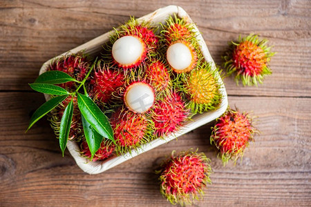 在盘子和木背景收获的红毛丹水果从花园，新鲜和成熟的红毛丹甜的热带水果剥皮的红毛丹与叶子 