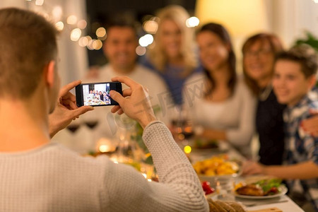庆祝、节日和人们的概念--拿着智能手机在晚宴上拍全家福。一名男子在晚宴上与家人合影