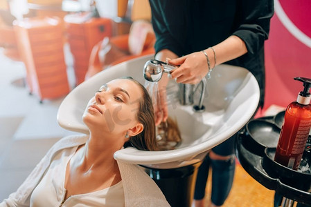 洗发用品海报摄影照片_美发师在洗脸盆、美发沙龙为顾客洗发。美容工作室的专业理发