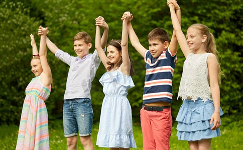 童年和友谊的概念--快乐的小朋友在夏令营里手牵手。快乐的孩子们在夏季公园里举起手