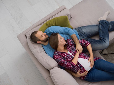怀孕的夫妇在沙发上放松。顶视图愉快的怀孕夫妇放松在沙发在家里