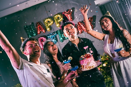 喇叭的摄影照片_亚洲朋友有乐趣在生日聚会在夜总会与生日蛋糕。活动和周年纪念的概念。人们的生活方式和友谊。