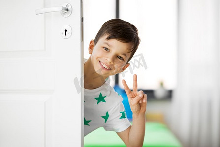 家里的门摄影照片_童年，乐趣和人的概念—快乐的小男孩在家里的门后显示和平。快乐的小男孩在家里门后显示和平