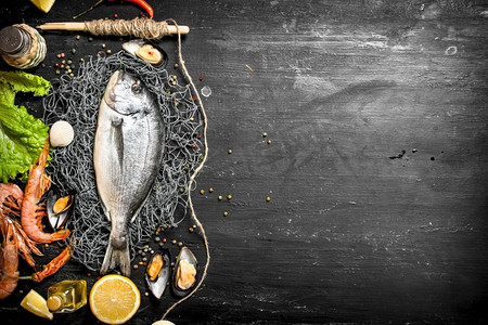 海鲜鱼摄影照片_新鲜的海鲜。鲜鱼配虾、柠檬和香料。在黑色黑板上..鲜鱼配虾、柠檬和香料。