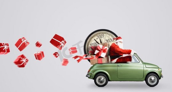 圣诞节到了摄影照片_圣诞节倒计时到了。汽车上的圣诞老人在送新年礼物和灰色背景的时钟。汽车上的圣诞老人倒计时